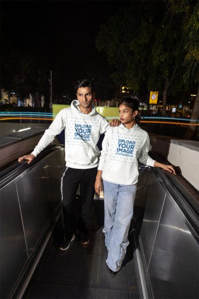Hoodie Mockup of a Serious Young Couple Standing on an Escalator with Blurry City Lights m56878
