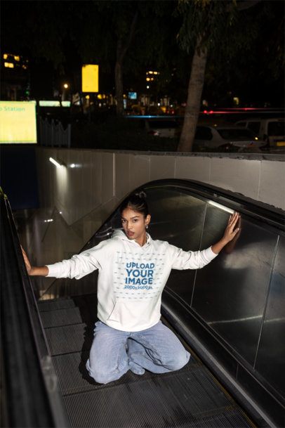 Hoodie Mockup Featuring a Young Woman Squatting on an Escalator in an Urban Setting at Night m56876