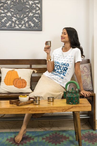 T-Shirt Mockup Featuring a Smiling Woman Holding a Cup on a Wooden Bench Indoors