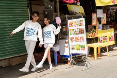 Matching Sweatshirt Mockup Featuring a Young Couple Holding Hands and Walking in a Street Market