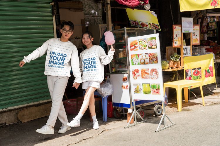 Matching Sweatshirt Mockup Featuring a Young Couple Holding Hands and Walking in a Street Market