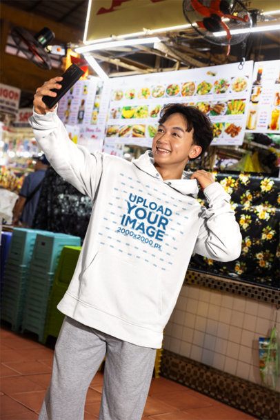 Hoodie Mockup Featuring a Smiling Young Man Taking a Selfie at a Food Market