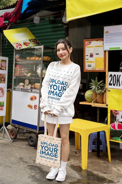 Sweatshirt and Tote Bag Mockup Featuring a Smiling Young Woman Standing at a Street Market