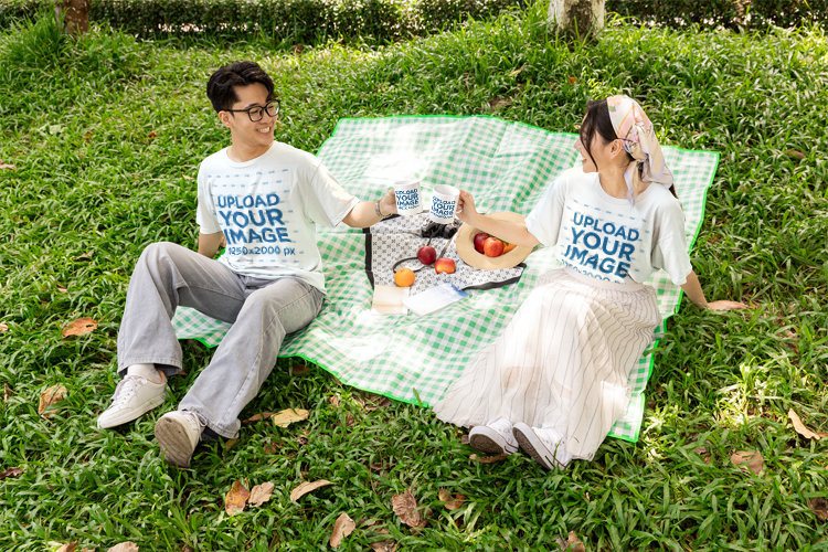 T-Shirt and Mug Mockup Featuring a Smiling Couple Toasting on a Picnic Blanket in a Park
