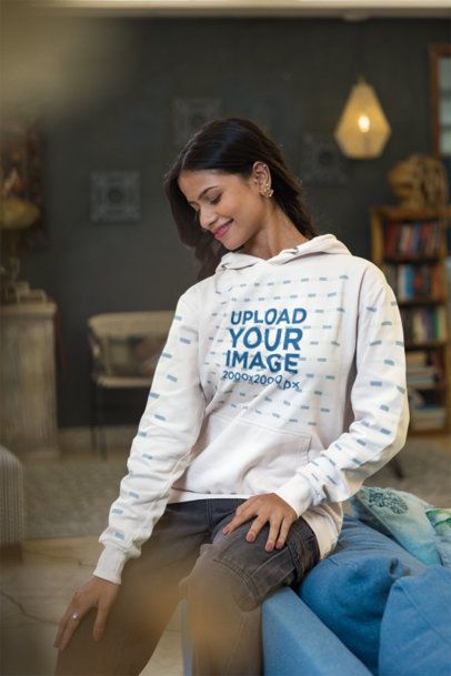 Hoodie Mockup Featuring a Smiling Woman Looking Down in a Cozy Tea Culture Inspired Living Room