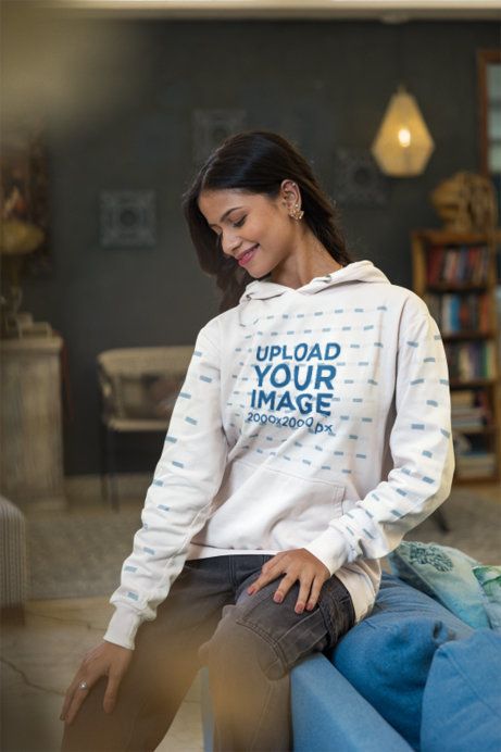 Hoodie Mockup Featuring a Smiling Woman Looking Down in a Cozy Tea Culture Inspired Living Room