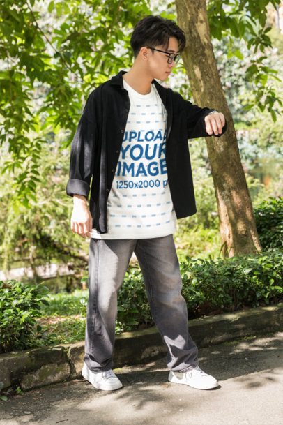 T-Shirt Mockup Featuring a Young Man Looking at His Watch in a Sunny Park