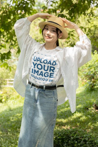 T-Shirt Mockup Featuring a Smiling Young Woman Holding Her Straw Hat in a Sunny Park