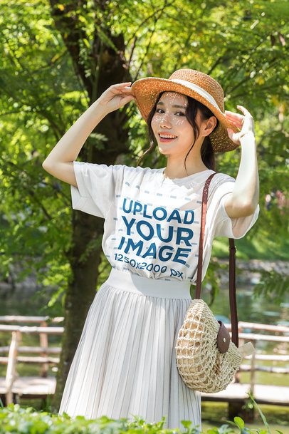 T-Shirt Mockup Featuring a Smiling Young Woman Adjusting Her Straw Hat in a Park