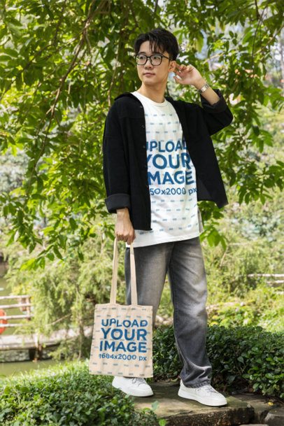 T-Shirt and Tote Bag Mockup Featuring a Young Man Looking Away in a Green Park