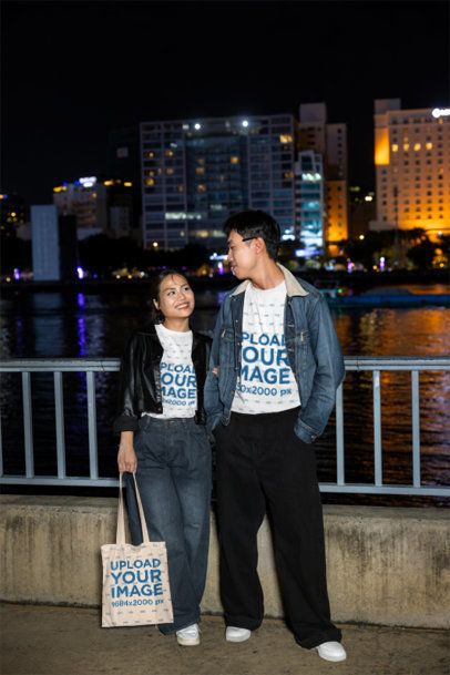 Couples T-Shirt and Tote Bag Mockup Featuring a Young Man and Woman Looking at Each Other by a River at Night