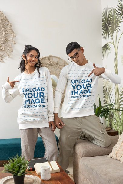 Pullover Mockup With a Young Couple Pointing at Their Shirts in a Boho Home Setting