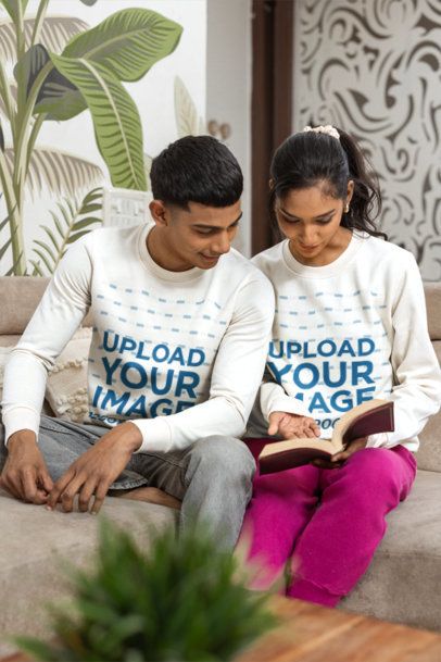 Couples Sweatshirt Mockup Featuring a Young Man and Woman Reading a Book on a Couch