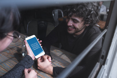 Mockup of a Woman Showing her iPhone to a Friend at a Restaurant