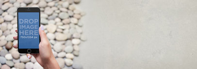 Mockup of an iPhone 6 Featuring a Holding Her iPhone Over Pebble Floor