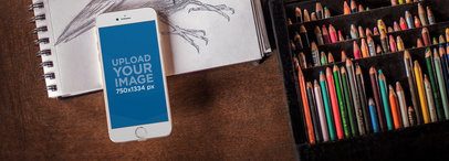 Mockup of a White iPhone 6 Lying on Top of a Drawing Sketchbook