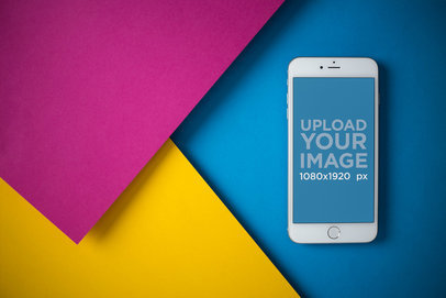 Mockup of an iPhone 8 Plus on a Blue Surface Next to Yellow and Pink Pasteboards