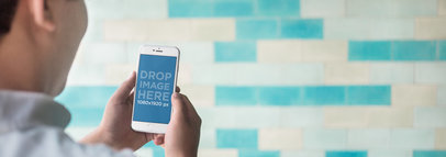 Man Holding an iPhone Over a Blue Tiled Wall Mockup Template