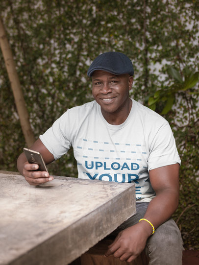 T-Shirt Mockup of a Senior Man Using his Smartphone on a Concrete Table 21431