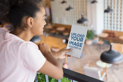 Mockup of a Woman Holding a Flyer Leaning Against a Railing