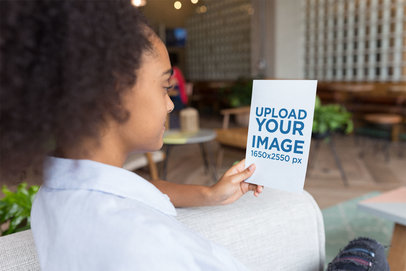 Mockup of a Woman Holding a Flyer Sitting on an Armchair