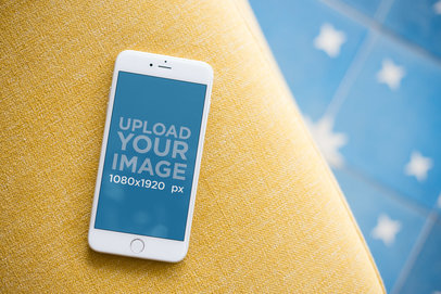 Mockup of a Silver iPhone 8 Plus Lying on Yellow Furniture