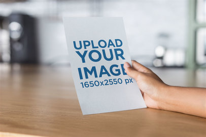 Mockup of a Hand Holding a Flyer on a Wooden Surface