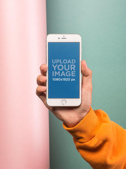 Mockup of a Hand Holding a Silver iPhone In Front of a Colorful Wall