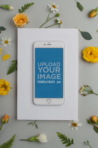 Mockup of a Silver iPhone Over a White Surface with Yellow and White Flowers in the Background