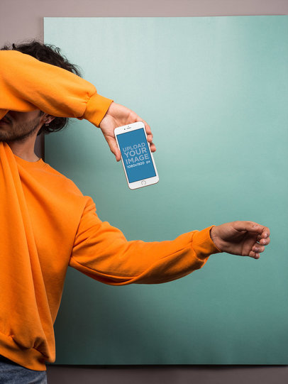 Silver iPhone 8 Plus Mockup Held by a Man in an Orange Sweatshirt Covering His Face
