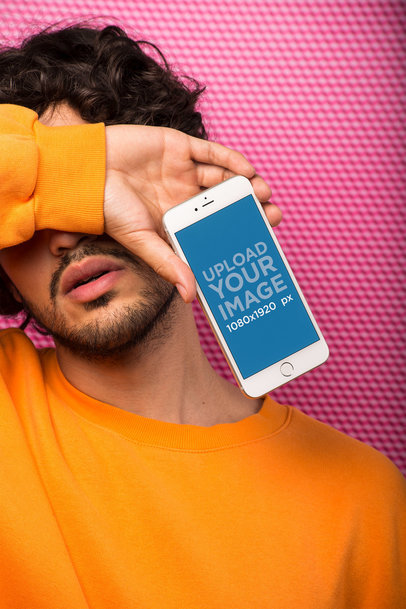 Mockup of a Bearded Man Covering His Face Holding a Silver iPhone In Front of a Textured Wall