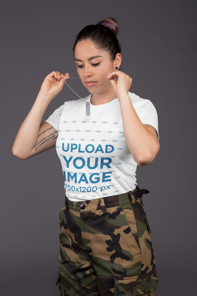 Crew Neck Tee Mockup Featuring a Female Veteran Wearing an Army Necklace Against a Gray Wall