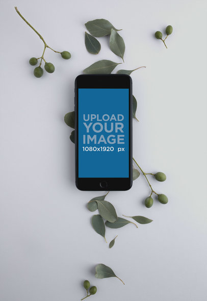 Mockup of a Space Gray iPhone on a White Surface with Leaves