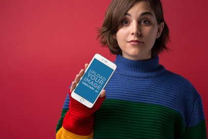 Silver iPhone 8 Plus Mockup Featuring a Surprised Girl Wearing a Striped Mock Neck Sweater Against a Red Wall 21828