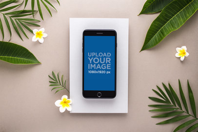 Mockup of a Gold iPhone 8 Plus Surrounded by Leaves and Plumeria Flowers
