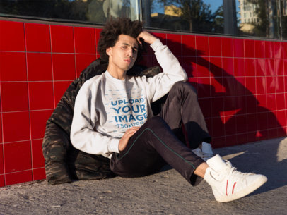 Mockup of a Concerned Man Wearing a Crewneck Sweatshirt Sitting Against a Red Tiles Wall 18334