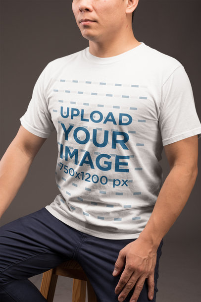 Crew-Neck Tee Mockup of a Guy in Blue Trousers Sitting on a Stool Against a Dark Gray Wall 21235