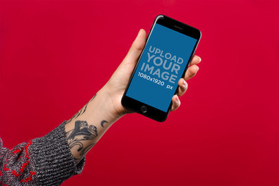 Mockup Featuring a Woman's Tattooed Arm Holding a Space Gray iPhone 8 Against a Red Surface 21958