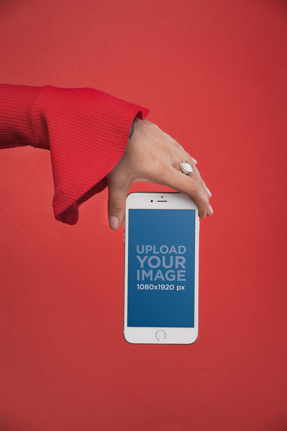 Mockup of a Woman’s Hand with a White Ring Showing an iPhone 8 Plus Against a Red Background