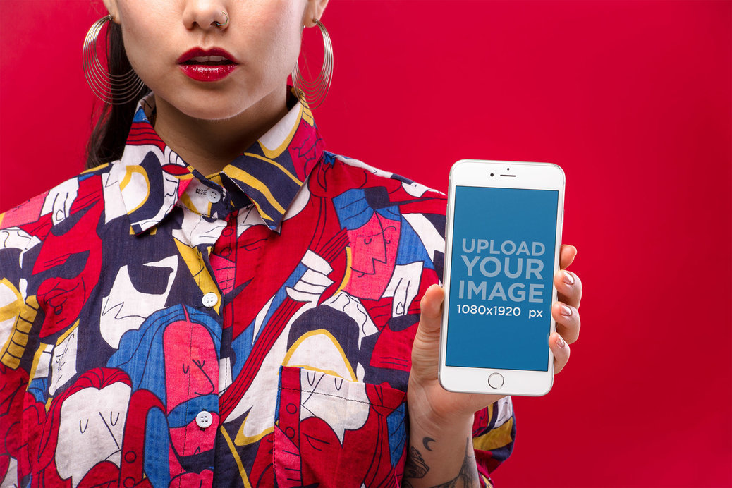 Mockup of a Woman with Hoop Earrings Wearing a Colorful Shirt Showing a Silver iPhone 8 Against a Red Background