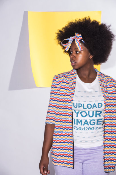 T-Shirt Mockup of a Young Woman with Afro Hair Wearing a Colorful Outfit Against a Square Yellow Paper