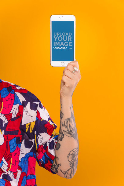 Mockup Featuring a Person with a Tattooed Arm Holding a Gold iPhone 8 Against a Light Orange Background 21963