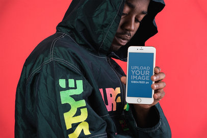 Mockup of a Man Showing a Silver iPhone 8 Against a Bright Red Wall
