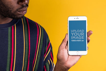 Mockup of a Man with a Holding an iPhone Against a Yellow Wall