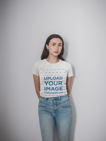 Mockup of a Woman Wearing a Round Neck Tee and Light Wash Jeans Posing Against a White Wall