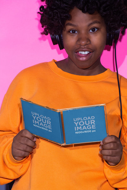 Mockup Featuring a Woman with an Afro Style and Orange Sweatshirt Holding a CD Cover 