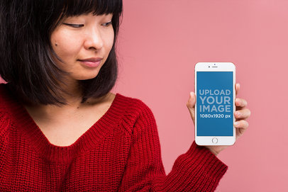 Gold iPhone 8 Mockup Featuring a Woman in a Red Sweater Against a Light Pink Wall 