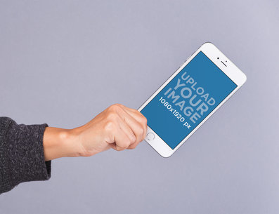 Mockup of a Hand Holding an iPhone 8 Plus in an Angled Position Against a Gray Surface