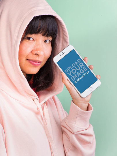 Mockup of a Woman Showing an iPhone 8 Plus Wearing a Pink Hoodie
