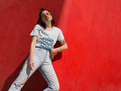 T-Shirt Mockup of a Woman with Jeans and Vintage Glasses Against a Red Wall 
